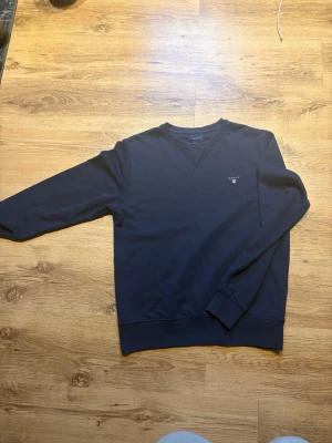 Mörkblå sweatshirt från Gant - En stilren mörkblå sweatshirt från Gant med rund halsringning och diskret logga broderad på bröstet. Tröjan har långa ärmar, ribbade muddar.