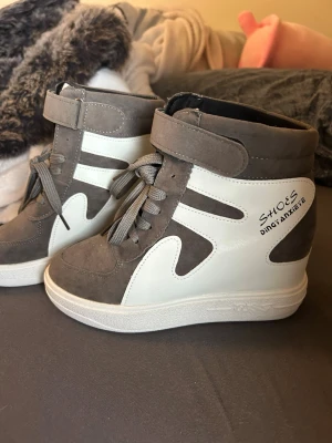 Gråvita high top sneakers med kardborre - Snygga high top sneakers i grått och vitt med både snörning och kardborreband. Skorna har en chunky sula och detaljer i mockaimitation samt texten 'SHOES Ding Anke' på sidan. Perfekta för dig som gillar streetstyle och vill sticka ut.