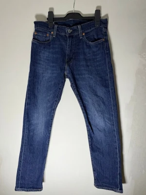Blå raka jeans från Levi's - Klassiska blå jeans från Levi's med rak passform och fem fickor. Jeansen har en snygg tvättad look, knappgylf och detaljer i kopparfärg. Tillverkade i slitstark denim med den ikoniska läderpatchen bak i midjan.