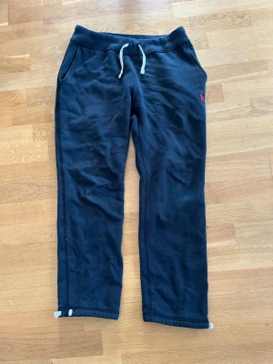 Svarta mjukisbyxor Ralph Lauren  - Säljer ett par svarta mjukisbyxor med vita dragsnören i midjan och fickor på sidorna. Byxorna har en liten röd logga på vänster sida och resår i midjan. Perfekta för chill dagar eller när du vill vara bekväm.