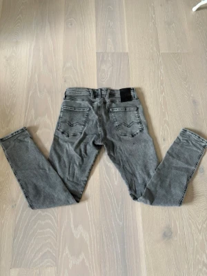 Grå Replay Hyperflex jeans - Säljer ett par gråa Replay Hyperflex jeans med klassisk femficksdesign och svarta detaljer. Jeansen har en slim passform och är tillverkade i stretchig bomullsmix för extra komfort. Perfekta för dig som gillar en modern och clean look. Pris går att diskutera. Vid intresse är det bara att höra av sig.