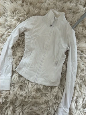 lululemon define jacket - Snygg vit cropped define jacket från Lululemon med figurnära passform och hög krage. Jackan har dragkedja framtill, två fickor med dragkedja och långa ärmar med tumhål. Perfekt för lager på lager och sportig stil. Fittar xs-s💖