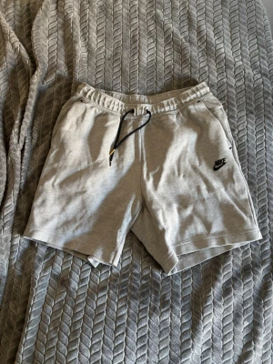 Gråa och svarta tech fleece sweatshorts från Nike - Få båda två för 250! Snygga gråa och svarta sweatshorts från Nike med svart logga på vänster ben. Shortsen har elastisk midja med snörning och sidofickor. Perfekta för chill eller träning, tillverkade i mjuk bomullsblandning för maximal komfort.