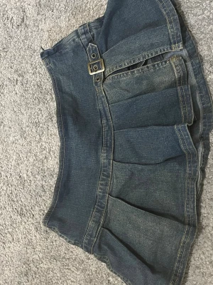 Miniskirt - Accepterar alla bud upp till 100kr upp till 24h efter annonsen blivit uppladdad!😍🙌Säljer en cool kort jeanskjol med plisserad nederdel och snyggt bälte med metallspänne framtill. Kjolen har klassisk blå denimfärg och kontrastsömmar som ger en trendig look. Perfekt för dig som gillar streetstyle och vill ha något unikt i garderoben. Köpt i new york för dyrt därav priset! 