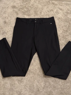 Svarta golfbyxor från J.Lindeberg - Snygga svarta golfbyxor från J.Lindeberg med rak passform och diskret logga vid fickan. Byxorna har bälteshällor och knappstängning. Perfekta för en clean och stilren look. Materialet känns mjukt och följsamt. Köpta för 900 förra säsongen!