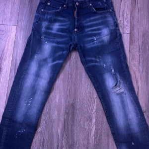 Slim jeans från Dsquared2  - Snygga slim fit jeans från Dsquared2 i mörkblå tvätt med slitningar och blekta detaljer. Klassisk femficksmodell med knappgylf och Dsquared2-logga på röd etikett. Jeansen har en modern, smal passform och är tillverkade i bomull med stretch.