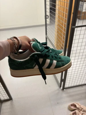 Adidas Campus gröna sneakers - Gröna Adidas Campus sneakers med klassiska vita ränder på sidan och vit logga på tungan. Skorna har en låg profil och är tillverkade i mocka med gummisula. Perfekt för dig som vill ha en cool och retro look.