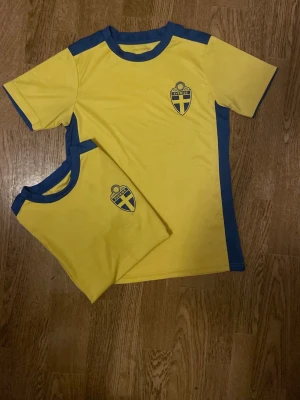 Svenska fotbollströjor gul/blå - Två gula fotbollströjor med blå detaljer och Sveriges landslagsemblem på bröstet. Tröjorna har rund hals och korta ärmar, tillverkade i ett lätt och snabbtorkande material som passar perfekt till träning eller match.