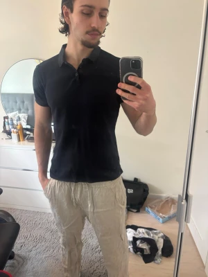 Svart kortärmad skjorta i bomull - En stilren svart skjorta med klassisk krage och knappar framtill. Skjortan har korta ärmar och är gjord i mjuk bomull som sitter slim på kroppen. Perfekt för en enkel och clean look.