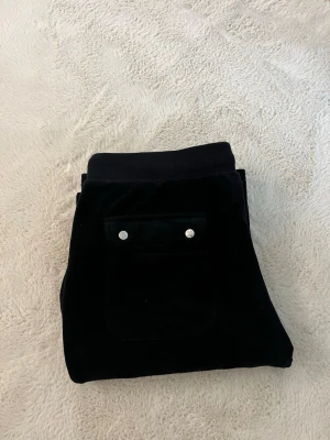 Svarta sammetsleggings med fickor - Snygga svarta leggings i mjuk sammet med två bakfickor som har silverfärgade knappar. De har en elastisk midja och smal passform, perfekta för en trendig och bekväm stil.