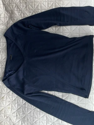 Mörkblå långärmad tröja - En enkel och stilren mörkblå långärmad tröja med trianglig halsringning. Tröjan har en smal passform och är tillverkad i ett mjukt, tunt material som passar perfekt till lager på lager. Perfekt basplagg för garderoben.