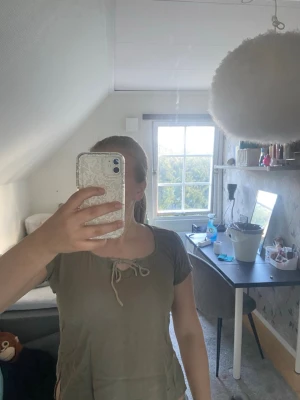 Olivgrön topp med snörning - Snygg olivgrön topp med kort ärm och snörning framtill vid halsen. Toppen har croppad passform och små slitsar i sidorna.  Sälj inte längre och är i bra skick!