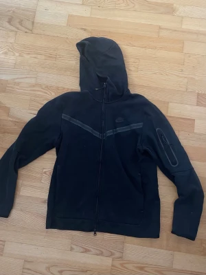 Nike tech hoodie svart - Svart Nike tech zip hoodie. Små defekter som tex på snörena som sitter på dragkedjorna. Köpt för cirka 1100kr nypris.