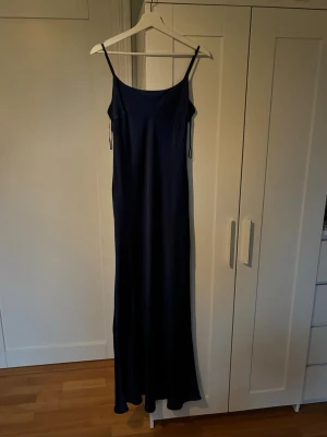 Mörkblå långklänning från Gina - Elegant mörkblå långklänning med smala axelband och rak siluett. Klänningen har en enkel, stilren design och är tillverkad i ett glansigt material som ger en lyxig känsla. Finns en liten fläck på framsidan till vänster, inte så synlig och går säkert att skrubba bort lätt. Priset går att prata om. Super snygg och älska verkligen den, passar tyvärr inte längre men super gullig och vacker💕🥂