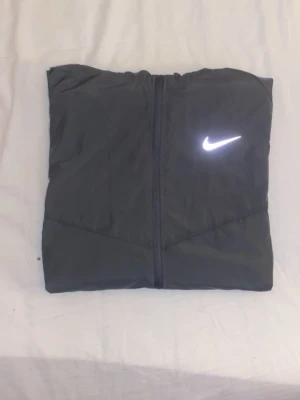 Nike Essential reflekterande löparjacka 🏃 - Denna Nike Essential-löparjacka är en lätt och funktionell vindjacka i grå – perfekt för träning i svalt väder eller svagt ljus. Den har en reflekterande Nike Swoosh-logga på bröstet och reflexdetaljer på ärmarna för ökad synlighet. Jackan är utrustad med huva med dragsko och två praktiska fickor med dragkedja. På insidan av kragen syns "NIKE RUNNING"-trycket, vilket understryker dess prestationsinriktade design ⭐️Skick: 9/10 🎨Färg; Grå 🎲 Storlek: M/L 