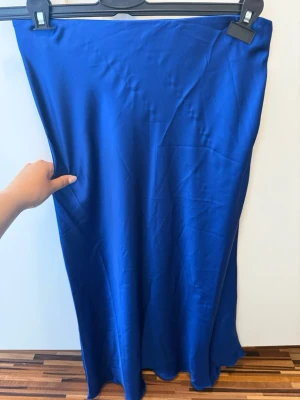 Blå långkjol från Lindex i satin - Snygg blå långkjol från Lindex i glansigt satinmaterial. Kjolen har en enkel och stilren design med rak passform och resår i midjan. Perfekt för dig som vill ha en statement piece i garderoben.