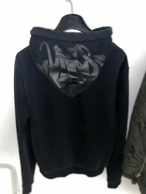 Svart syna world hoodie - Säljer en svart hoodie från synawrld med stort tryck på huvan i en cool graffiti-stil.