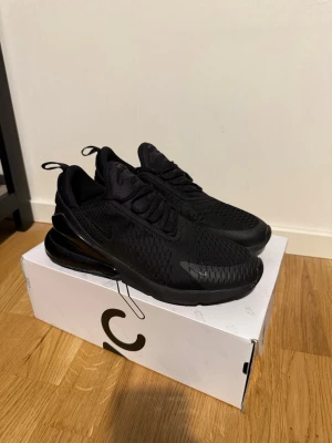Svarta Nike Air Max 270 sneakers - Snygga helsvarta Nike Air Max 270 sneakers med mesh-ovandel och stor synlig Air-enhet i hälen. Skorna har en sportig siluett, dragflikar bak och framtill samt diskreta loggor på sidan och plösen. Perfekta för dig som gillar stilrena och bekväma sneakers. Helt oanvända och nya.