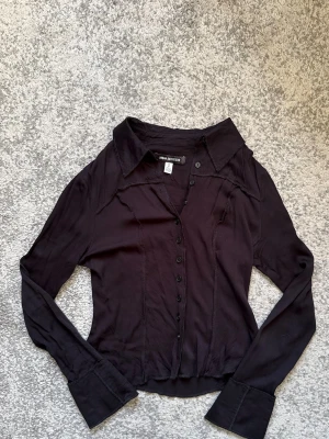 Svart långärmad skjorta - Stilren svart skjorta med lång ärm och klassisk krage. Skjortan har knappar framtill och är tillverkad i ett mjukt, lätt material som ger en snygg passform. Perfekt för dig som gillar en enkel men trendig look.