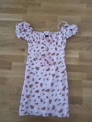 Blommig kortklänning från Bik Bok - Söt ljusrosa kortklänning från Bik Bok med orange blommönster, puffärmar och snörning framtill. Klänningen har en smickrande passform och är perfekt för varma dagar. Tillverkad i ett lätt och luftigt material. Storlek S. Oanvänd