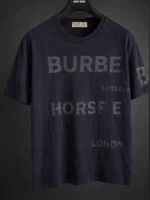 Burberry t-shirt - Snygg mörkblå t-shirt från Burberry med diskret tryck i samma ton på både fram- och baksidan. Klassisk rund halsringning och korta ärmar. Perfekt för dig som gillar stilrena plagg med exklusiv känsla och subtil branding.
