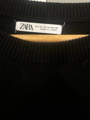 Svart basic tröja från Zara - En enkel svart tröja från Zara med rund halsringning och långa ärmar. Tröjan har ribbade muddar vid hals, ärmslut och nederkant. Perfekt att matcha med jeans eller kjol för en clean look.