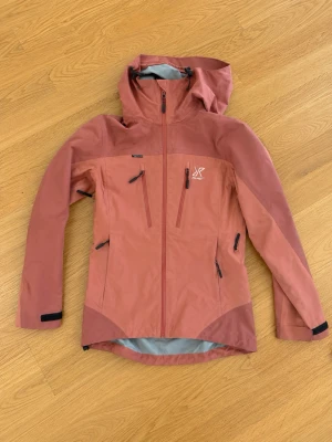 Rosa vindjacka med huva - Snygg vindjacka i två nyanser av rosa med huva och dragkedjor framtill. Jackan har flera praktiska fickor med dragkedja och justerbara ärmslut med kardborre. Perfekt för blåsiga dagar och outdoor-aktiviteter.