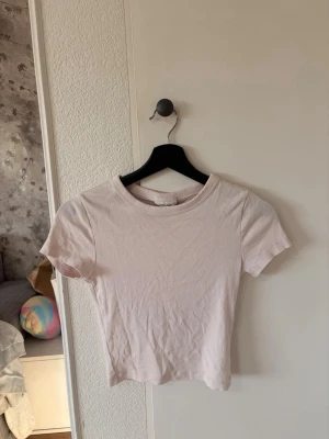 Ljusrosa t-shirt - Säljer en enkel och stilren ljusrosa t-shirt med rund halsringning och korta ärmar. Ganska kort o tajt 