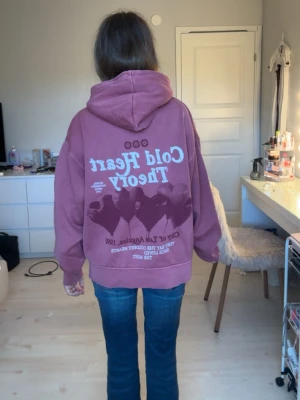 Rosa hoodie med tryck och huva - Säljer en oversized rosa hoodie med vit text och tryck både fram och bak. Texten säger 'Cold Heart Theory' och har coola grafiska detaljer. Hoodien har en stor ficka framtill och en rejäl huva. Perfekt för en avslappnad och trendig look.