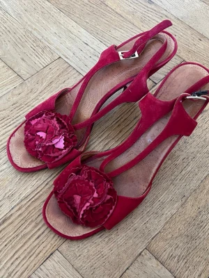 Röda pumps med blomdetalj Chie Mihara - Snygga röda pumps i mocka från Chie Mihara🥰🥰. Skorna har en stor dekorativ blomma framtill och en elegant klack. Använda, men bra skick! 