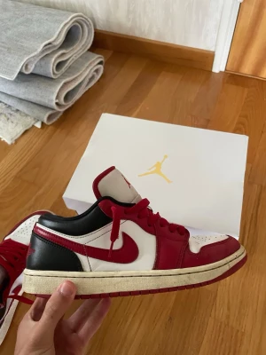 Air Jordan 1 Low röd/vit/svart - Säljer ett par Air Jordan 1 Low sneakers i rött, vitt och svart läder. Klassisk Nike Swoosh i rött på sidan, röda skosnören och vit mellansula. Ikonisk Jumpman-logga på plösen och lågt skaft för en clean look.
