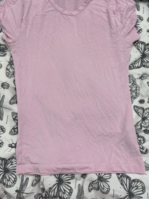 Ljusrosa basic t-shirt i bomull - En enkel och stilren ljusrosa t-shirt med rund halsringning och korta ärmar. Tillverkad i mjuk bomull som känns skön mot huden. Perfekt att matcha med jeans eller kjol för en avslappnad look. 