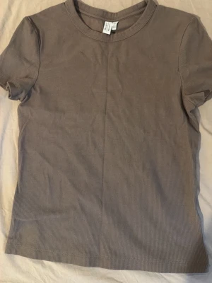 Beige ribbad t-shirt  - En enkel och stilren beige t-shirt med ribbad struktur. T-shirten har korta ärmar och rund halsringning, perfekt för en avslappnad look. Materialet känns mjukt och följsamt mot huden.