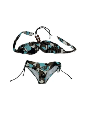 Blommig bikini i blå och brun med pärlor - Snygg bikini med blommigt mönster i blått, svart, brunt och vitt. Överdelen har halterneck med träpärlor och knyt i nacken, medan underdelen har snörning i sidorna. Båda är storlek 46-48 men de är små i storleken och toppen går att justera bak och kring hals genom att knyta den. Oanvända.