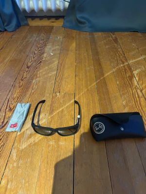Svarta Ray-Ban solglasögon rektangulära - Snygga svarta solglasögon från Ray-Ban med rektangulär form och mörka glas. Kommer med originalfodral och putsduk. Perfekta för soliga dagar och ger en cool look till din outfit. Kvitto tillkommer också för den delen.