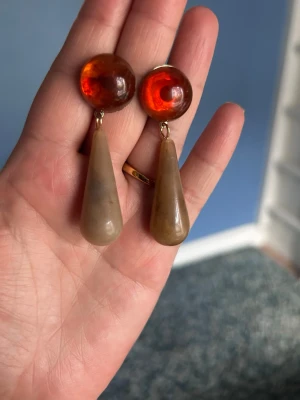 Bruna droppformade statementörhängen - Unika örhängen med rund, bärnstensfärgad topp och droppformad beige/brun hängande del. Örhängena har en cool retrovibe och är tillverkade i plast eller resin. Perfekta för dig som vill sticka ut med accessoarerna.