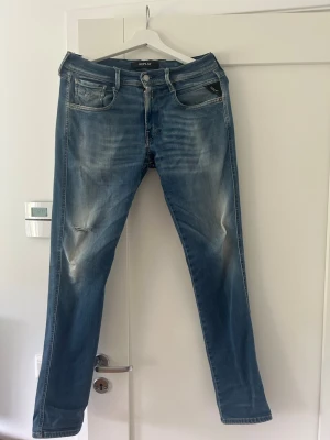 Blå Replay jeans med slitningar - Säljer ett par blå jeans från Replay med snygga slitningar och tvättade detaljer. Klassisk femficksmodell med raka ben och normal midja. Jeansen har en liten reva på vänster lår och är tillverkade i bomull med en skön stretch. Perfekta för en avslappnad look. Har även en liten reva vid skrevet. Kontakta vid eventuella frågor!
