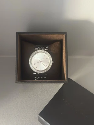Silverfärgad klocka från Michael Kors - Stilren helt oanvänd klocka från Michael Kors i silver med rund urtavla och länkarmband. Urtavlan är enkel och elegant med diskreta markeringar och en glittrig ram runt. Perfekt accessoar för dig som gillar klassisk och tidlös design.