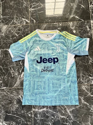 Juventus Adidas matchtröja blå - Säljer en Juventus matchtröja från Adidas i ljusblått med vitt och gula detaljer. Tröjan har ett unikt mönster, korta ärmar och tryck med Jeep och Visit Detroit på bröstet. Perfekt för fotbollsträning eller att bära till vardags.
