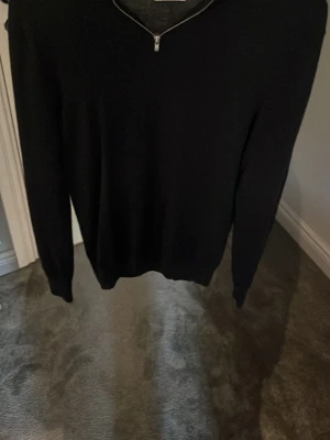 Svart stickad tröja med dragkedja - Snygg svart stickad tröja från Studio Total med halv dragkedja vid halsen. Tröjan har lång ärm och en enkel, stilren design som passar till det mesta. Perfekt för dig som gillar minimalistisk stil och vill ha något bekvämt och trendigt.