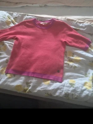 Rosa stickad tröja Pernilla Wahlgren - Säljer en rosa stickad tröja från Pernilla Wahlgren med lila ribbade muddar vid hals, ärmslut och nederkant. Tröjan har en strukturerad stickning och kortare ärmar. Perfekt för dig som gillar färg och vill ha något unikt i garderoben.