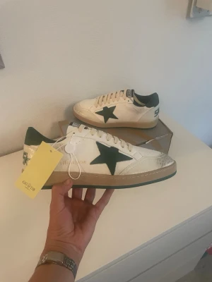Golden Goose ballstar - Golden Goose sneakers i vitt läder med grön stjärndetalj på sidan och grön häl. Klassisk låg modell med beige sula och vita skosnören. Märkets logga syns på plösen och hälen. Kommer med originalkartong och dustbag.