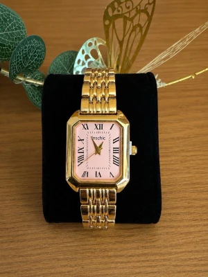 Guldig fyrkantig klocka från Vinschic - Stilren klocka från Vinschic med fyrkantig urtavla i ljusrosa och romerska siffror. Armbandet är i guldtonad metall med länkdesign. Perfekt accessoar för dig som vill ha en elegant och trendig look.