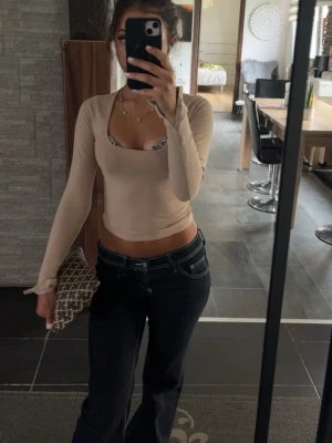 Beige croppad långärmad topp - Trendig beige croppad topp med lång ärm och djup urringning. Tillverkad i ett stretchigt material som sitter tight mot kroppen. Perfekt att styla med jeans eller kjol för en snygg look.