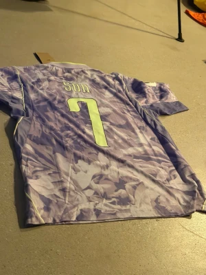 Lila Korea fotbollströja Nike Son 7 - Säljer en lila fotbollströja från Nike med namn Son och nummer 7. Tröjan har ett mönstrat kamouflage i olika lila nyanser, gula detaljer och Korea-märke på bröstet. Perfekt för dig som gillar fotboll och vill sticka ut på planen.