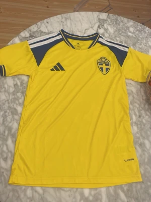 Svensk landslagströja Adidas gul 2026 vm tröja - Gul svensk landslagströja från Adidas med blå detaljer och vita ränder på axlarna. 