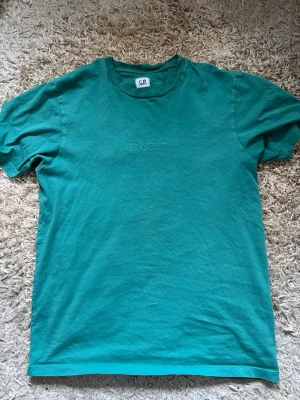 Grön t-shirt från C.P. Company - Snygg grön t-shirt från C.P. Company med diskret broderad logga på bröstet. Klassisk rund halsringning och korta ärmar. Tillverkad i mjuk bomull som känns skön mot huden. Perfekt till jeans eller shorts för en clean och enkel stil.