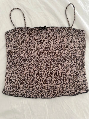 Leopardmönstrad linnetopp med rosett - Säljer en leopardmönstrad linnetopp med tunna axelband och en liten rosett framtill från Bershka. Lappen är avklippt, men skulle gissa att den är i storlek S.Toppen har en beige bas med svarta leopardfläckar och är perfekt för dig som vill sticka ut. Materialet känns mjukt och lätt, perfekt för varma dagar.