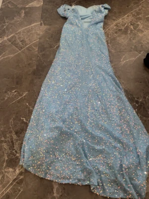 Ljusblå glittrig långklänning - Säljer en ljusblå långklänning med glittriga paljetter över hela klänningen. Klänningen har korta ärmar och en elegant, svepande form. Perfekt för bal eller festliga tillfällen. Materialet känns mjukt och skimrande. Klänningen är borttagen från shein men jag köpte den för 600 men säljer den för 500 och den är bara använd en gång 