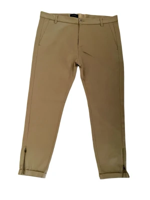 Beige chinos från Gabba - Snygga beige chinos från Gabba med klassisk rak passform och diskreta fickor fram. Byxorna har bälteshällor, knappgylf och dragkedjor vid bensluten för en modern touch. Tillverkade i ett mjukt och bekvämt bomullsmaterial. Storlek 52 (motsvarar storlek 36/32) 